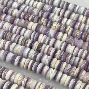May include: A strand of purple and white shell beads. The beads are round and have a natural, organic look.