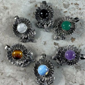 May include: Six silver sunflower pendants with different colored gemstone centers. The gemstones are black, white, green, brown, blue, and purple.