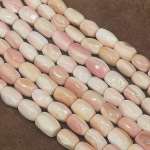 May include: A strand of pink and white shell beads, each bead is oval shaped and has a smooth, polished finish.