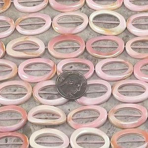 May include: A strand of oval-shaped shell beads with a pink and white color pattern. The beads have a hole in the center and are strung together with a thin thread. The beads are approximately 1 inch in length.