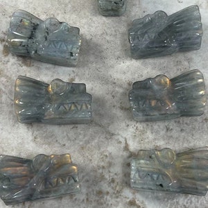 May include: Eight iridescent grey dragon head carvings made of labradorite gemstone. The carvings are approximately 1 inch in length and feature detailed facial features.