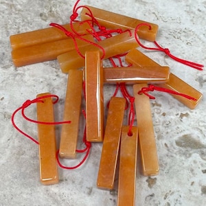 May include: A group of orange and yellow rectangular stone charms with red string attached to each one. The charms are stacked on top of each other.