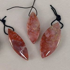 May include: Three red agate leaf-shaped pendants with black cords. The pendants have a marbled pattern with white and gold accents.