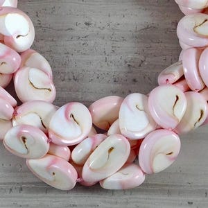 Peut inclure: Un collier de perles en coquillage rose et blanc. Les perles sont de forme ovale et ont un aspect naturel et organique.