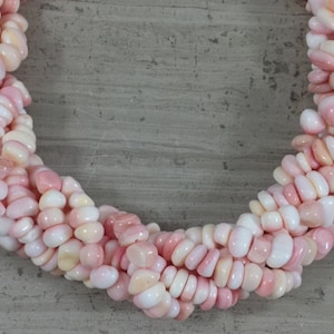 Könnte beinhalten: Eine Strähne aus rosa und weißen Muschelperlen mit glatter, abgerundeter Form. Die Perlen sind zu einer Halskette oder einem Armband zusammengefügt.
