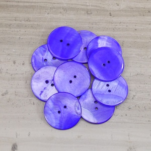 May include: A group of 10 round, blue, iridescent buttons with two holes each. The buttons are made of mother of pearl and have a shiny finish.