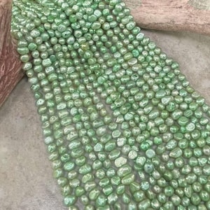 May include: A collection of light green freshwater pearls, each with an irregular shape and a glossy finish. The image also shows a section of a brown antler and a light grey surface.