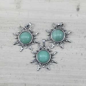 May include: Three silver sun pendant charms with green gemstone cabochons. Each charm features a sunburst design with a round stone in the center.