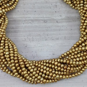 May include: A strand of golden pearl beads, arranged in a circular pattern on a gray background.
