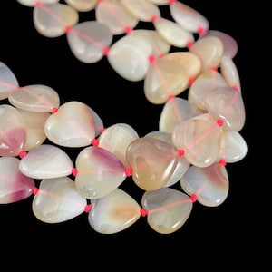 May include: A strand of heart-shaped agate beads with pink and white stripes. The beads are strung on a red cord.