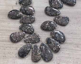 Puede incluir: Una hebra de cuentas de piedra de ágata negra y blanca. Las cuentas tienen una forma irregular y un patrón moteado.