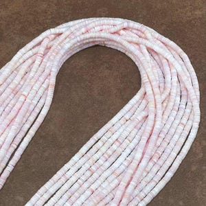 以下が含まれることがあります： ピンクと白の貝殻ビーズの連なり。ビーズは平らな円盤状で、つなぎ合わされており、流れるような質感のある外観を作り出しています。カラーパレットはソフトで、ピンクと白のバリエーションがあります。ビーズはおそらくジュエリー作りに使用されます。