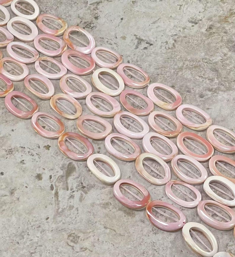 May include: A strand of pink and white oval shell beads with a hole in the centre of each bead. The beads are arranged in rows and are strung on a white cord.