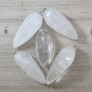 Może przedstawiać: Pięć przezroczystych wisiorów z kryształu kwarcowego z srebrnymi kółkami. Wisiorek ma kształt łzy i gładkie, polerowane wykończenie.