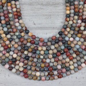 May include: A strand of round, multi-coloured gemstone beads. The beads are a mix of brown, red, grey, and white with a variety of patterns.