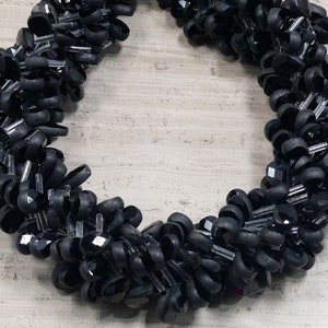 May include: A black beaded necklace made of faceted glass beads and black rubber beads. The beads are arranged in a spiral pattern.