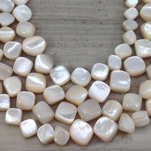 May include: A strand of white iridescent shell beads, each bead is a smooth, rounded square shape.