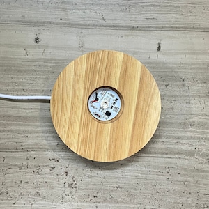 May include: A round wooden base with a light brown finish. The base has a small white circle in the center with black text and a red circle.