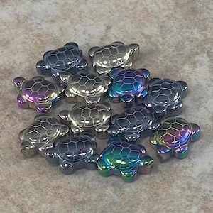 May include: A collection of iridescent turtle-shaped beads. The beads have a metallic sheen, with colors shifting from blue to purple and green. Each turtle has a textured shell design.