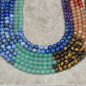 May include: A set of three ceramic mugs with a speckled, cream-colored glaze. Each mug features a different hand-painted design: a blue and green leaf, a yellow flower, and a red berry. The mugs have a simple, modern design.