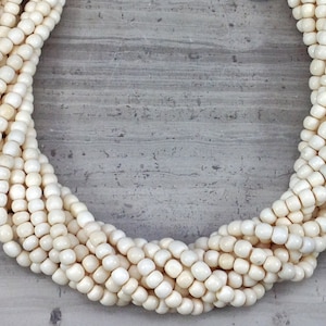 May include: A strand of white bone beads, arranged in a circle on a gray background.