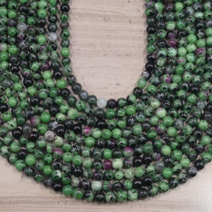 May include: A strand of green, black, and pink gemstone beads. The beads are round and have a smooth, polished finish.