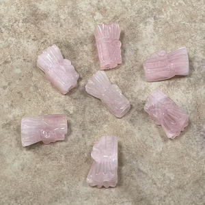 May include: Seven pink carved crystal beads in various shapes, including a flower, a leaf, and a geometric design. The beads are smooth and polished, with a translucent appearance.