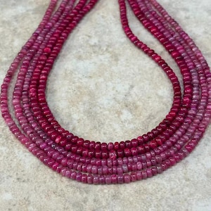 May include: Six strands of pink and magenta gemstone beads. The beads are small and round, with a polished finish. The strands are arranged in a layered pattern, creating a gradient effect from light pink to deep magenta.