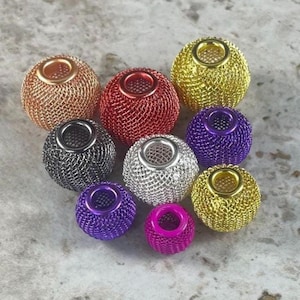 Peut inclure: Un assortiment de perles sphériques en maille métallique de différentes couleurs. Les perles comprennent du cuivre, du rouge, du noir, de l'argent, du violet, du rose et de l'or. Chaque perle a un trou central.