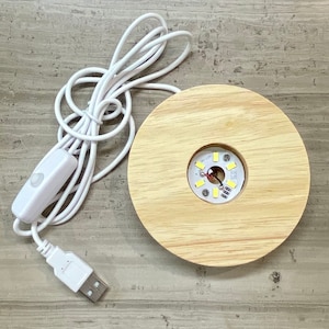 以下が含まれることがあります： 白のUSBケーブル、スイッチ、コネクタが付いた、丸い明るい色の木製LEDライトベース。ベースには、小さな回路基板と明るい白色LEDライトを備えた円形のくぼみがあります。ケーブルはコイル状になっています。