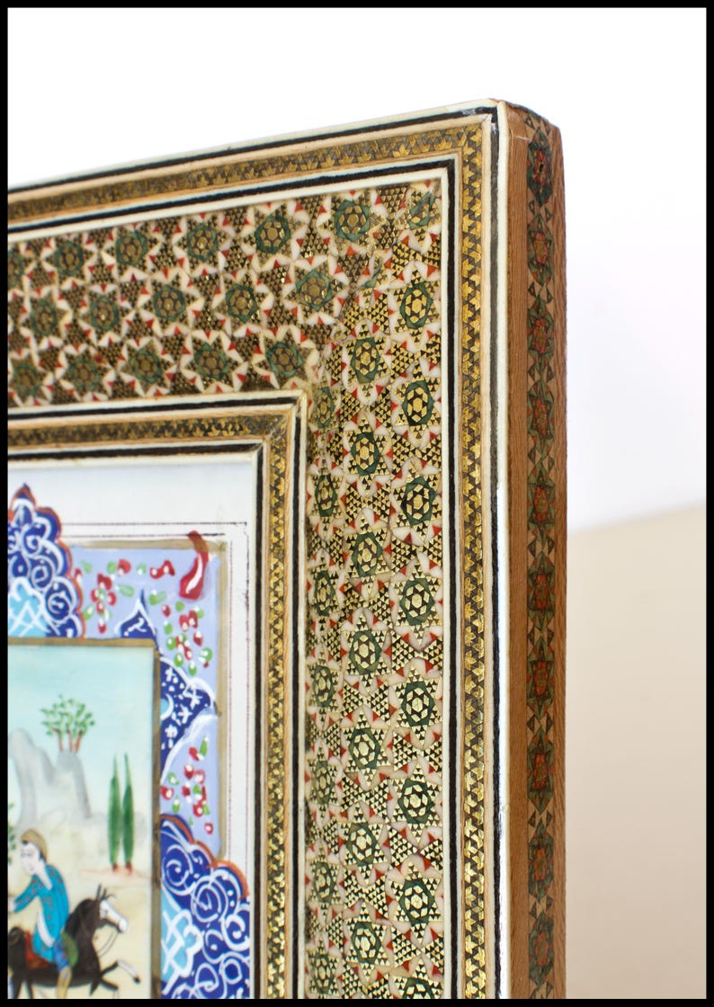 May include: Close-up of a decorative frame with intricate mosaic and gold detailing. The frame features a detailed pattern of green, red, and gold geometric shapes. The artwork within the frame depicts a scene with figures on horseback and landscape elements.