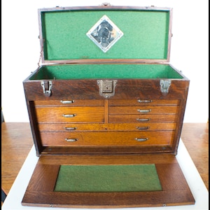May include: An antique wooden toolbox with multiple drawers and a green felt lining. The toolbox has a hinged lid with a diamond-shaped mirror inset.