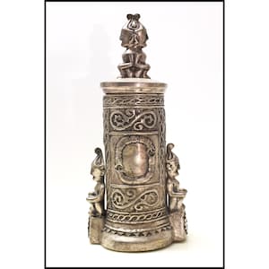 May include: A silver-colored, ornate decorative object with a cylindrical body and a detailed top. The body features intricate patterns and two small figures. The top has a detailed design with multiple faces.