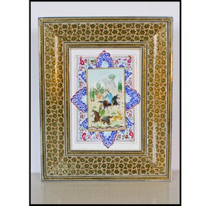 May include: An ornate framed artwork featuring a miniature painting of figures on horseback. The frame has a gold and green floral pattern, with a blue and white decorative border around the painting. The painting depicts a landscape scene.