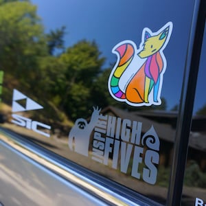 May include: A car window with several stickers. The stickers are of a fox, a sloth, a triangle, and a text that says "Inspire High Fives".