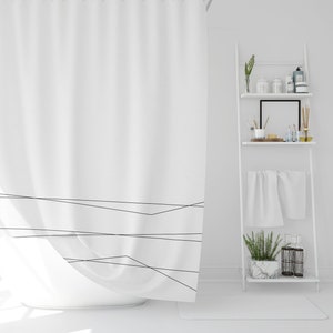 May include: A white shower curtain with a simple black geometric design. The curtain is hanging in a white bathroom with a white shelf unit holding various items.