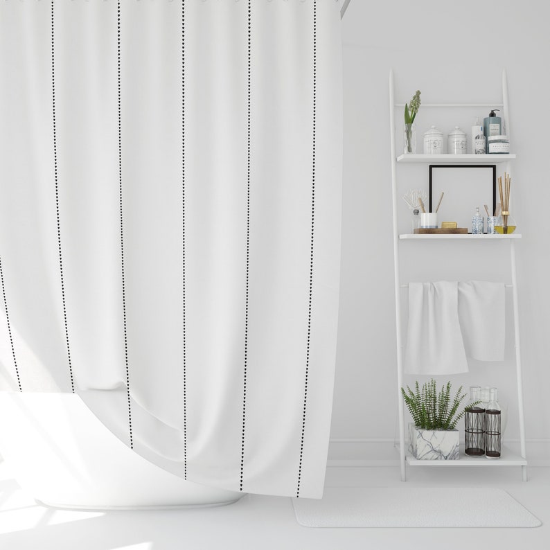 May include: White shower curtain with black dotted lines. The curtain is hanging in a bathroom with a white tiled floor and a white shelf unit with towels and toiletries.