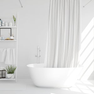 May include: White bathtub with a white shower curtain with black vertical stripes. The shower curtain is partially pulled back to reveal the bathtub. The bathtub is in a white bathroom with a white shelf unit in the background.