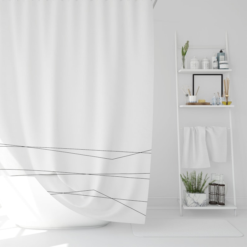 May include: A white shower curtain with a simple black geometric design. The curtain is hanging in a white bathroom with a white shelf unit holding various items.