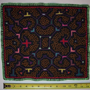 May include: A rectangular textile with a black background and a complex pattern of orange, purple, green, red, pink, and yellow shapes. The edges are trimmed with green and red stitching. The textile measures approximately 35.5 cm wide.