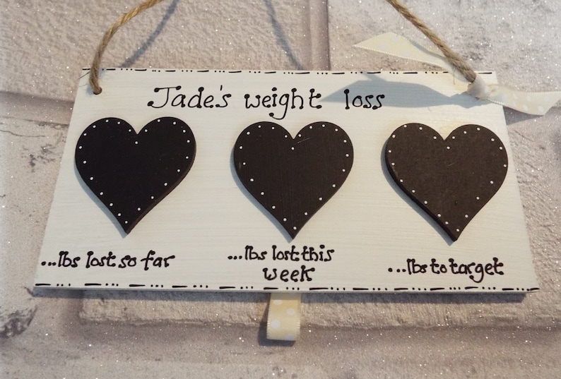 May include: White wooden sign with three black hearts, each with white polka dots. The sign reads "Jade's weight loss... lbs lost so far... lbs lost this week... lbs to target".