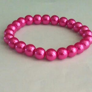 May include: A pink pearl bracelet with a simple design. The bracelet is made of small, round pearls that are strung together on a clear elastic cord.