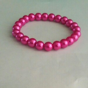 May include: A pink pearl bracelet with a simple design. The bracelet is made of small, round pearls that are strung together on a clear elastic cord.