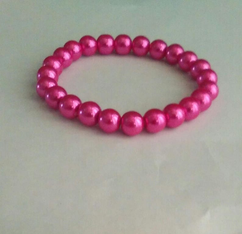 May include: A pink pearl bracelet with a simple design. The bracelet is made of small, round pearls that are strung together on a clear elastic cord.