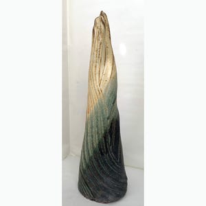 May include: A tall, ceramic sculpture with a textured, layered design. The colors transition from a light beige at the top to shades of green and dark blue at the base. The artwork has a unique, organic shape.