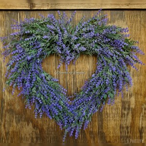 May include: A heart-shaped lavender wreath with purple flowers and green leaves. The wreath is hanging on a wooden door. The text "Wreaths by Vongsai" is visible in the centre of the wreath.