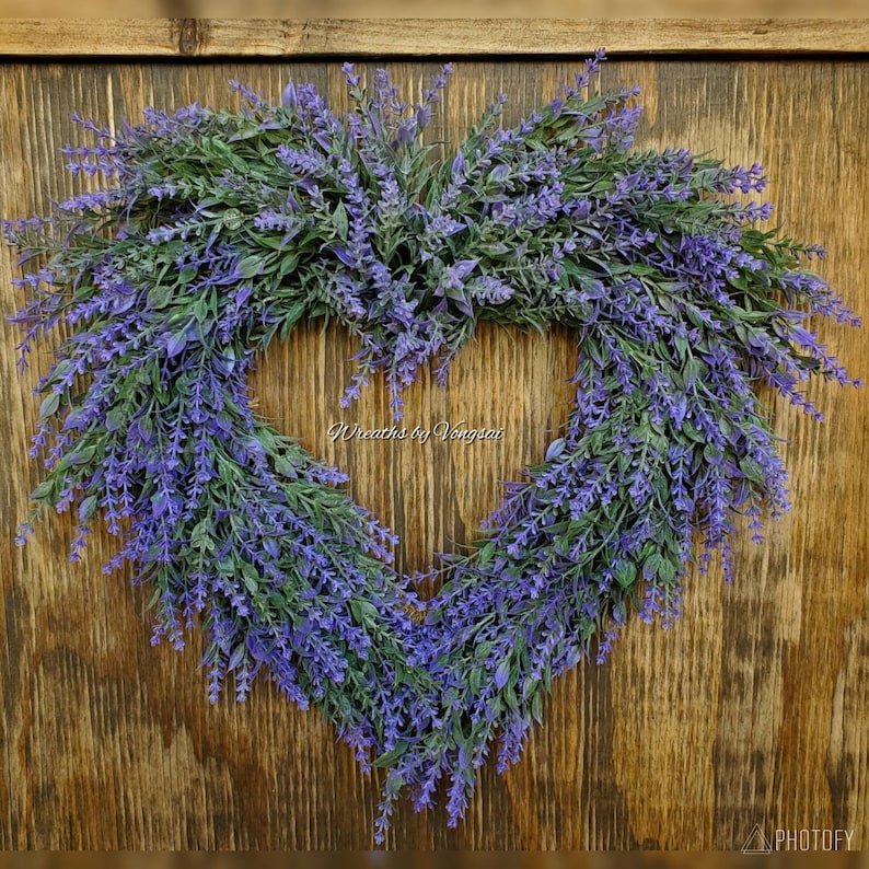 May include: A heart-shaped lavender wreath with purple flowers and green leaves. The wreath is hanging on a wooden door. The text "Wreaths by Vongsai" is visible in the centre of the wreath.