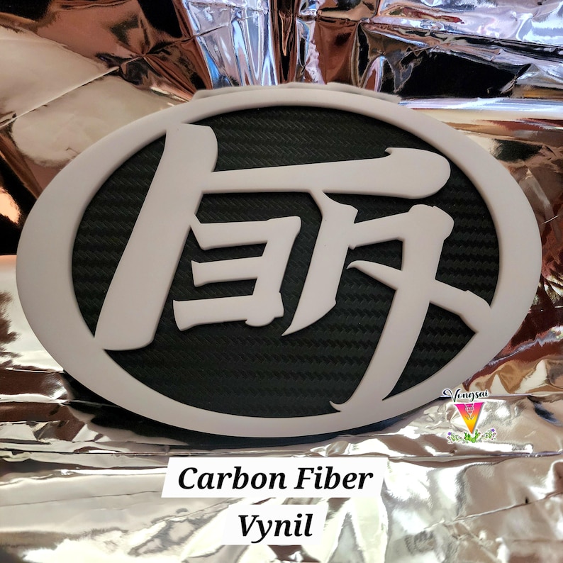 May include: An oval-shaped emblem featuring a white border and white Japanese kanji characters set against a black carbon fiber textured background. The design is clean and bold, showcasing a high-contrast aesthetic with a matte white finish.