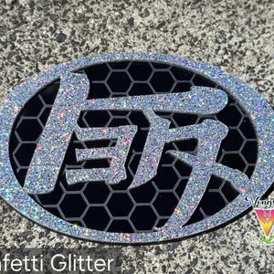 May include: An oval-shaped emblem featuring a silver confetti glitter border and Japanese kanji characters in the center. The background of the emblem consists of a black honeycomb pattern. The text Vongsai is visible in the bottom right corner.