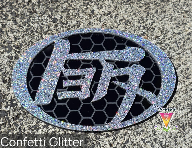 May include: An oval-shaped emblem featuring a silver confetti glitter border and Japanese kanji characters in the center. The background of the emblem consists of a black honeycomb pattern. The text Vongsai is visible in the bottom right corner.
